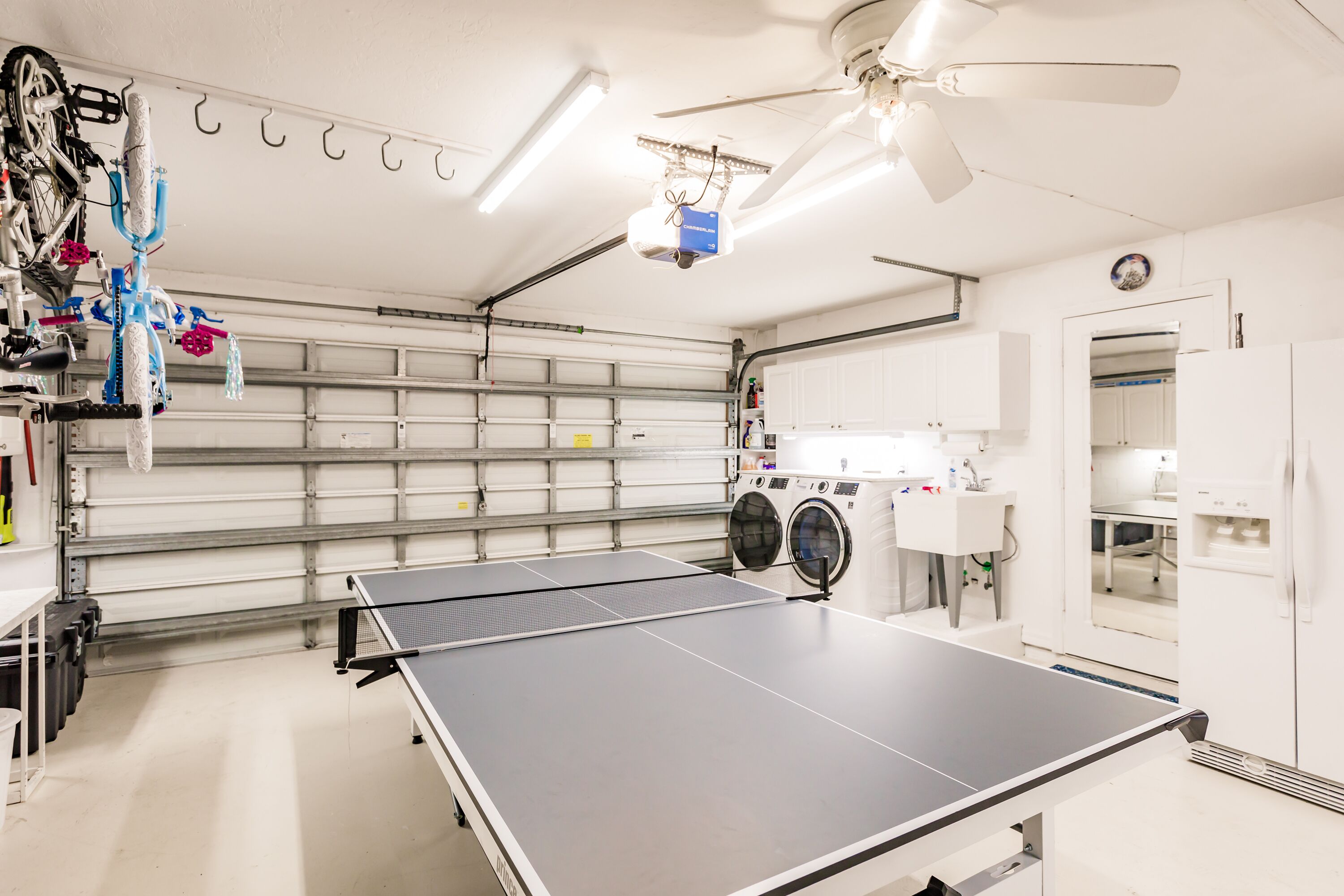 A clean, well-lit indoor space with a ping pong table, a ceiling fan, and a washing machine.