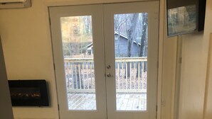 Una habitación con piso de madera, un tapete estampado, un taburete mullido y una puerta corrediza de vidrio que da a una terraza.