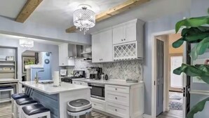 Una cocina moderna con armarios blancos, una isla central con taburetes y un salpicadero de baldosas en patrón de espiga.