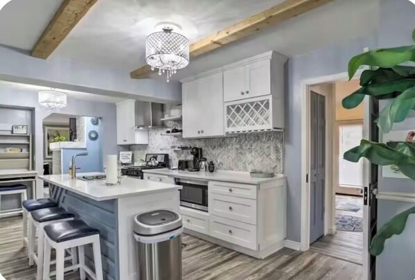 A modern kitchen with white cabinetry, a central island with stools, and a herringbone tile backsplash.