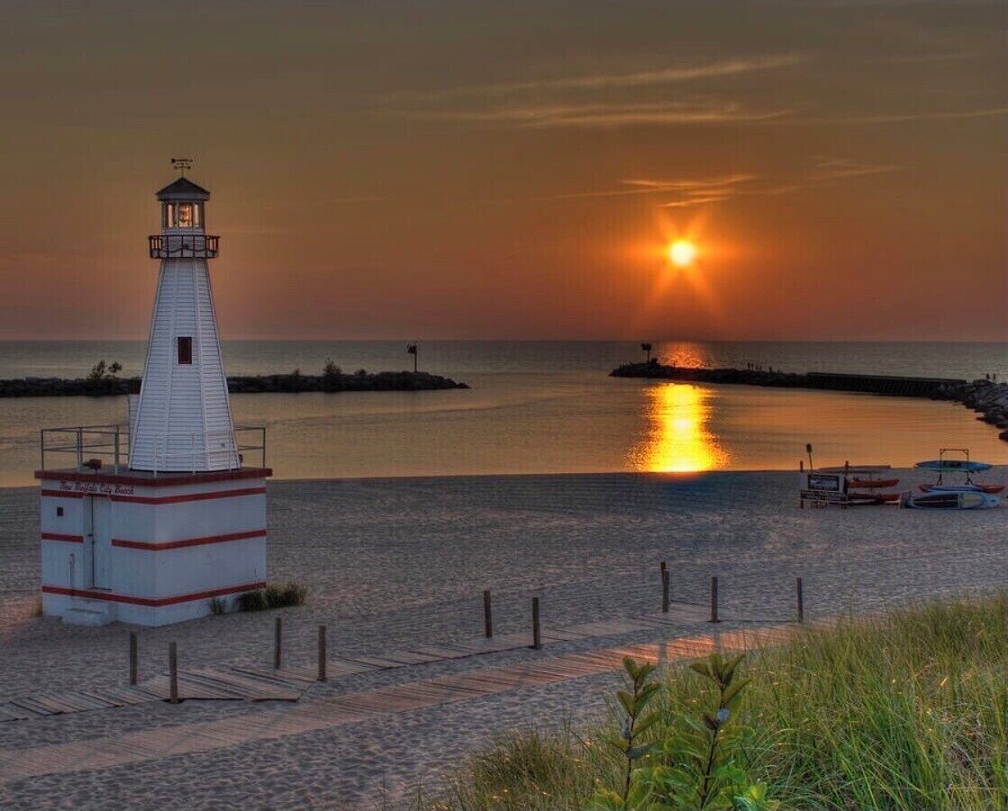 A lighthouse at sunset with a clear view of the water and boats.