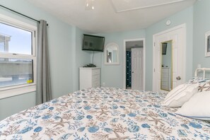 Une chambre à coucher avec un lit, une commode, un téléviseur, un miroir et une fenêtre avec des rideaux.