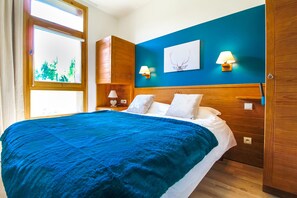 Una camera da letto con un letto grande, una testata in legno, due lampade ai comodini, un’opera d’arte appesa al muro e una finestra con vista sugli alberi.