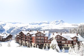 Un chalet à plusieurs étages, avec une piste de ski en arrière-plan.