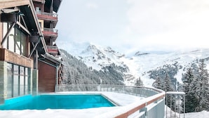En pool omgiven av snö, ett trädäck och utsikt över ett berg.