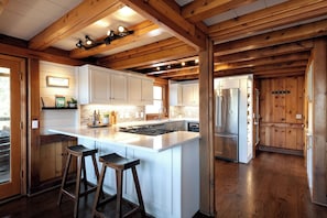 A kitchen with wooden beams, white cabinetry, a central island with stools, and stainless steel appliances.