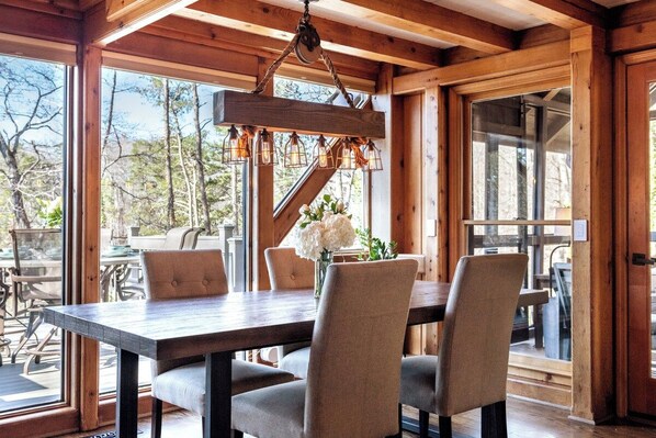 Open dining room with rustic beams, lush greenery & lake views — the perfect setting for cozy family breakfasts or candlelit dinners at the Hygge House on Lake Lanier in Gainesville, GA.