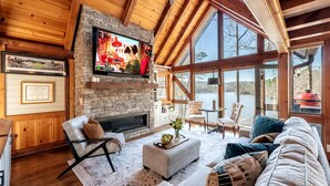 Una sala de estar acogedora con chimenea de piedra, asientos confortables y ventanas amplias que dan a la naturaleza.