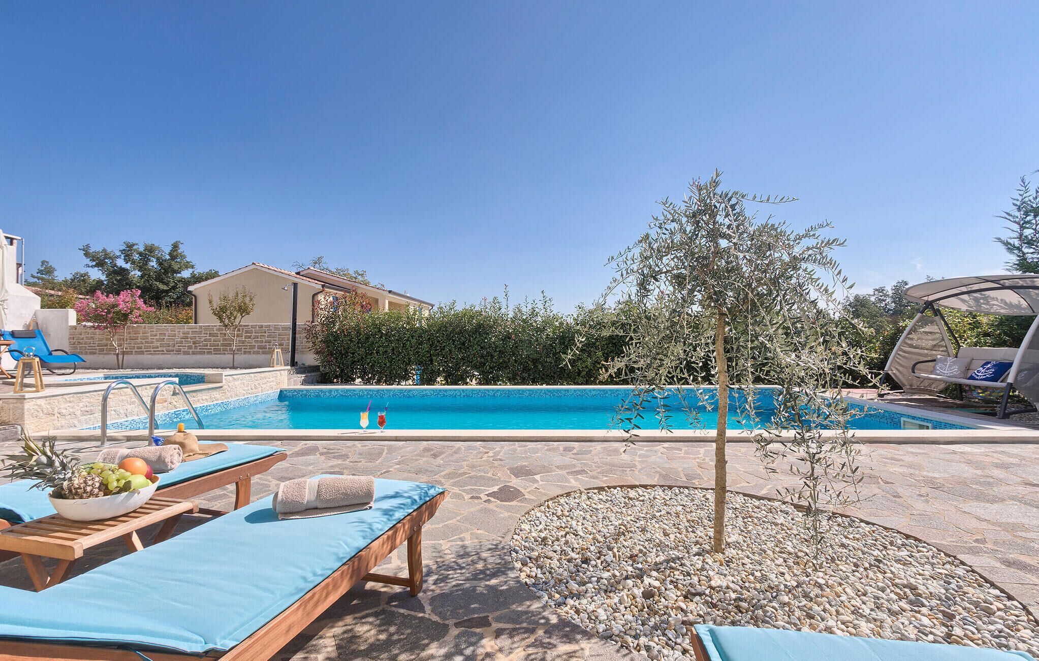 A pool area with lounge chairs, a small tree, and a building in the background.
