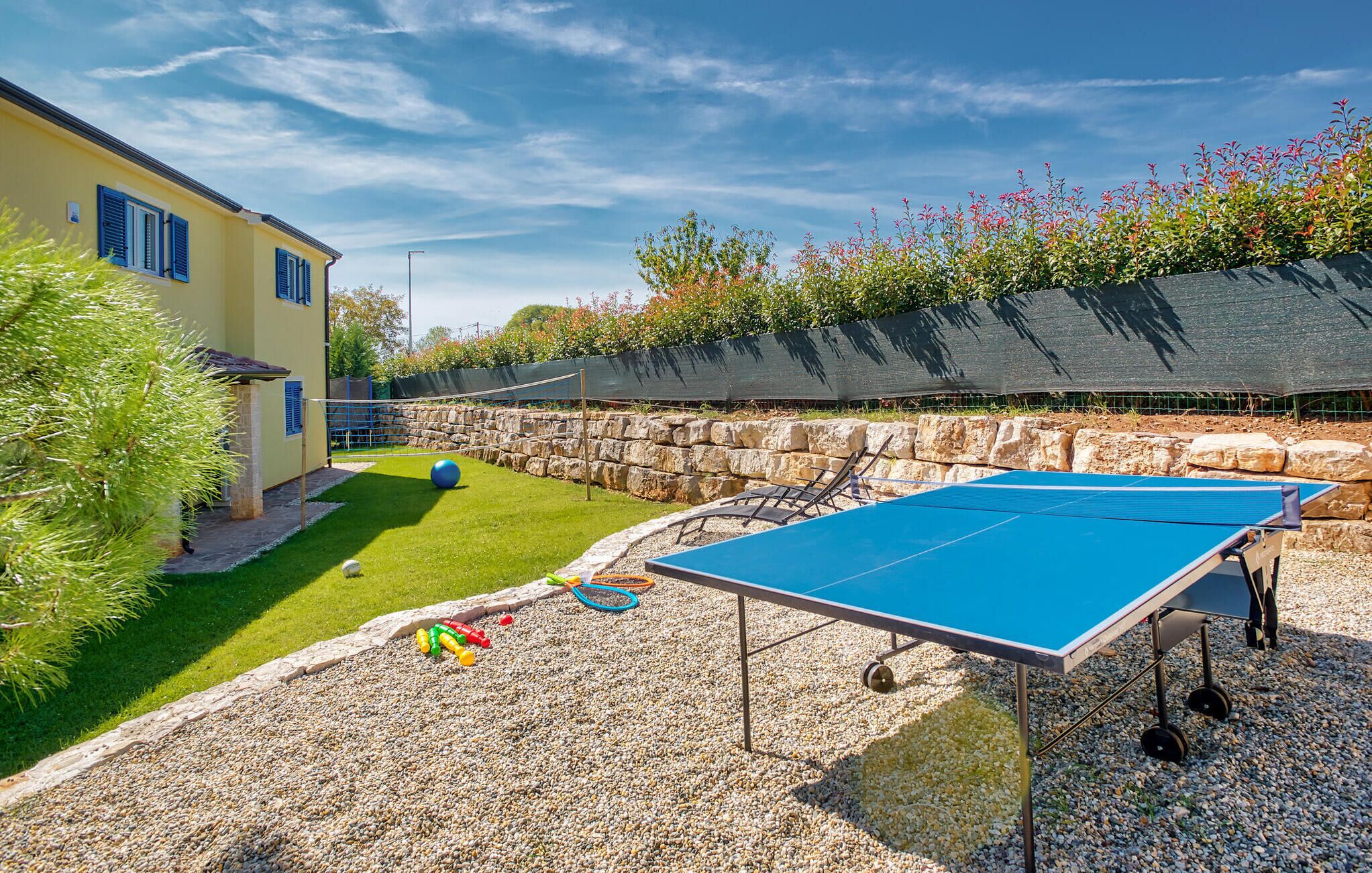 Ein Pingpongtisch in einem Garten mit einer Steinmauer, einer Rasenfläche und einem Haus im Hintergrund.