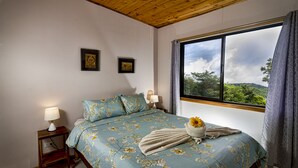 A bedroom with a bed, a nightstand, a window with a view of trees, and two framed pictures on the wall. - Private Attached 1BR in Monteverde - Gulf Views - Sleeps 3 (Monteverde)