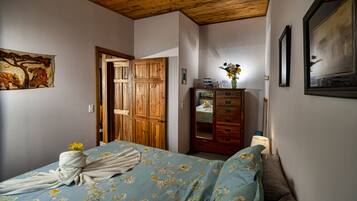 A bedroom with a wooden ceiling, a bed with floral bedding, a wooden wardrobe, and a painting on the wall.