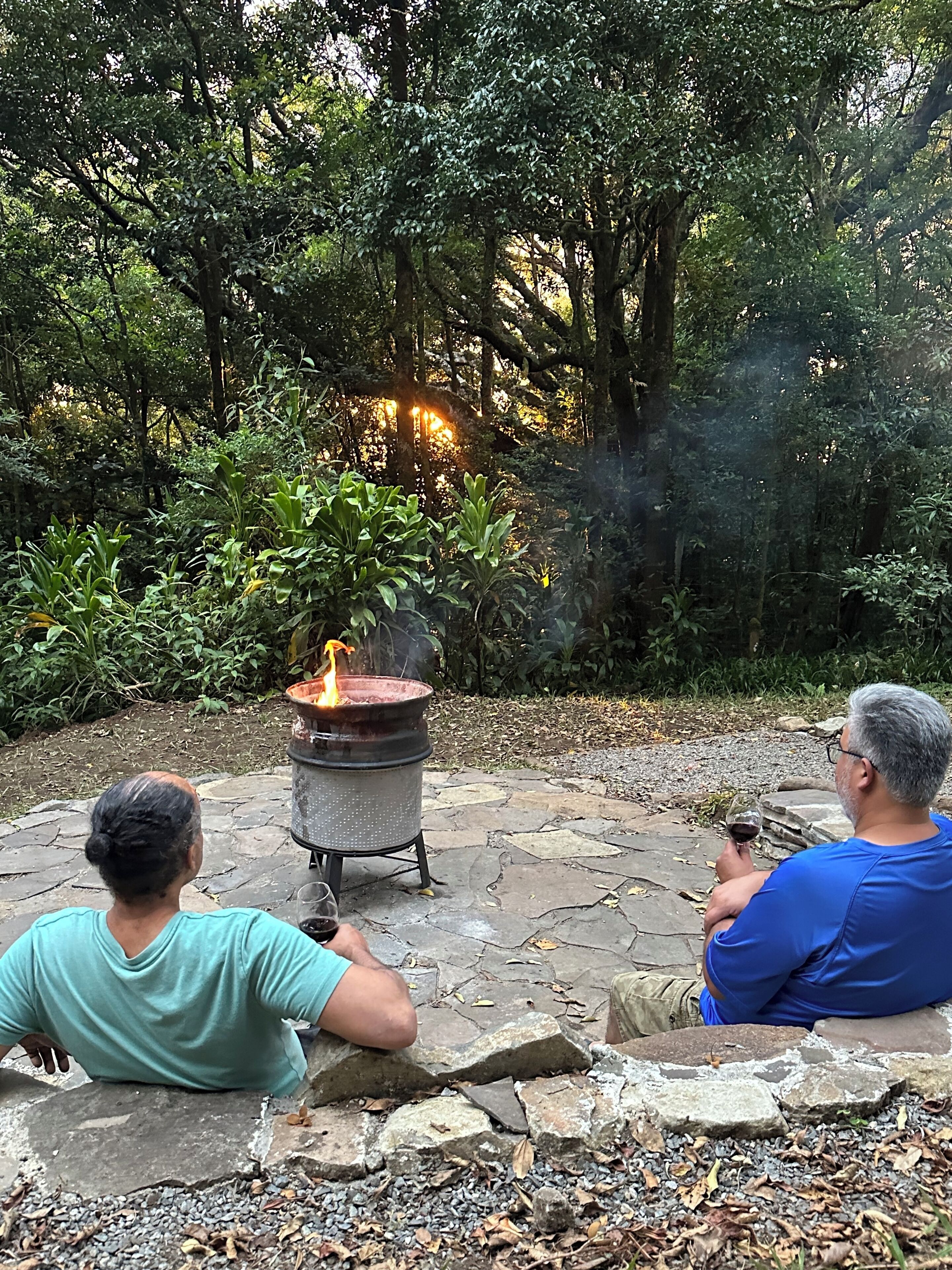 Two people sitting on stone steps in a garden with a wood-burning stove in the background.
