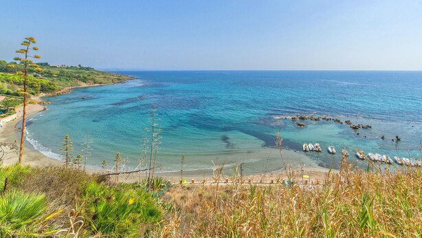 Un paysage côtier avec une eau turquoise cristalline, une plage de sable et des bateaux ancrés près du rivage.