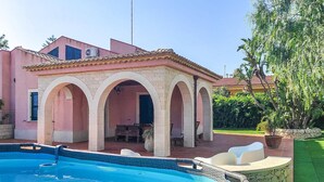 Une maison avec une piscine, un patio couvert avec des meubles d’extérieur et un jardin avec des arbres.