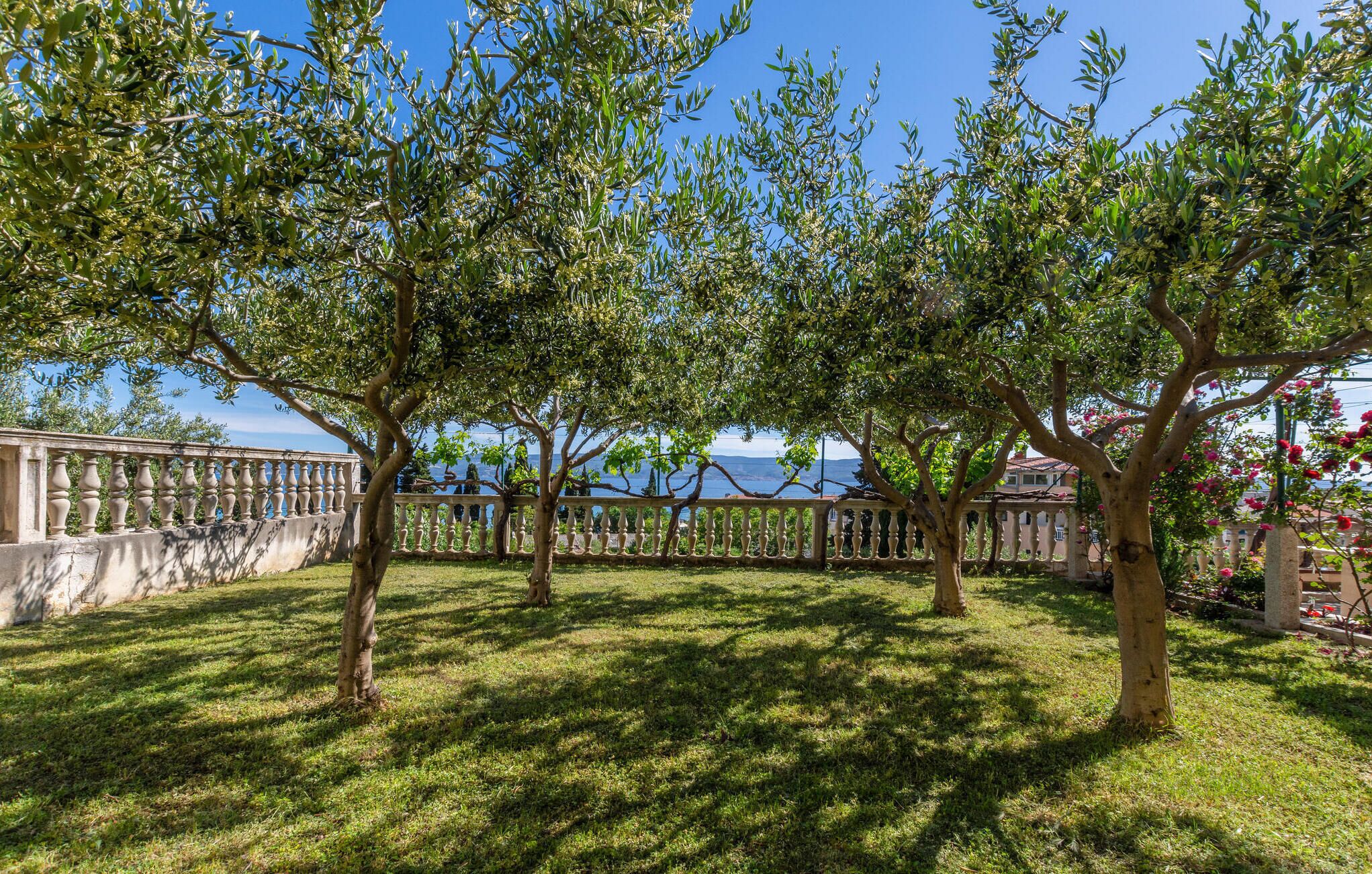 A garden with a stone balustrade, trees, and a view of the sea.