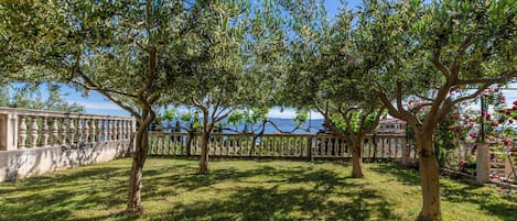 A garden with a stone balustrade, trees, and a view of the sea.