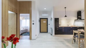 Een moderne hotelkamer met een houten garderobe, een bed met een blauw-wit geweven vloerkleed, een hal die leidt naar een keuken met een eethoek en een uitzicht buiten door een raam.