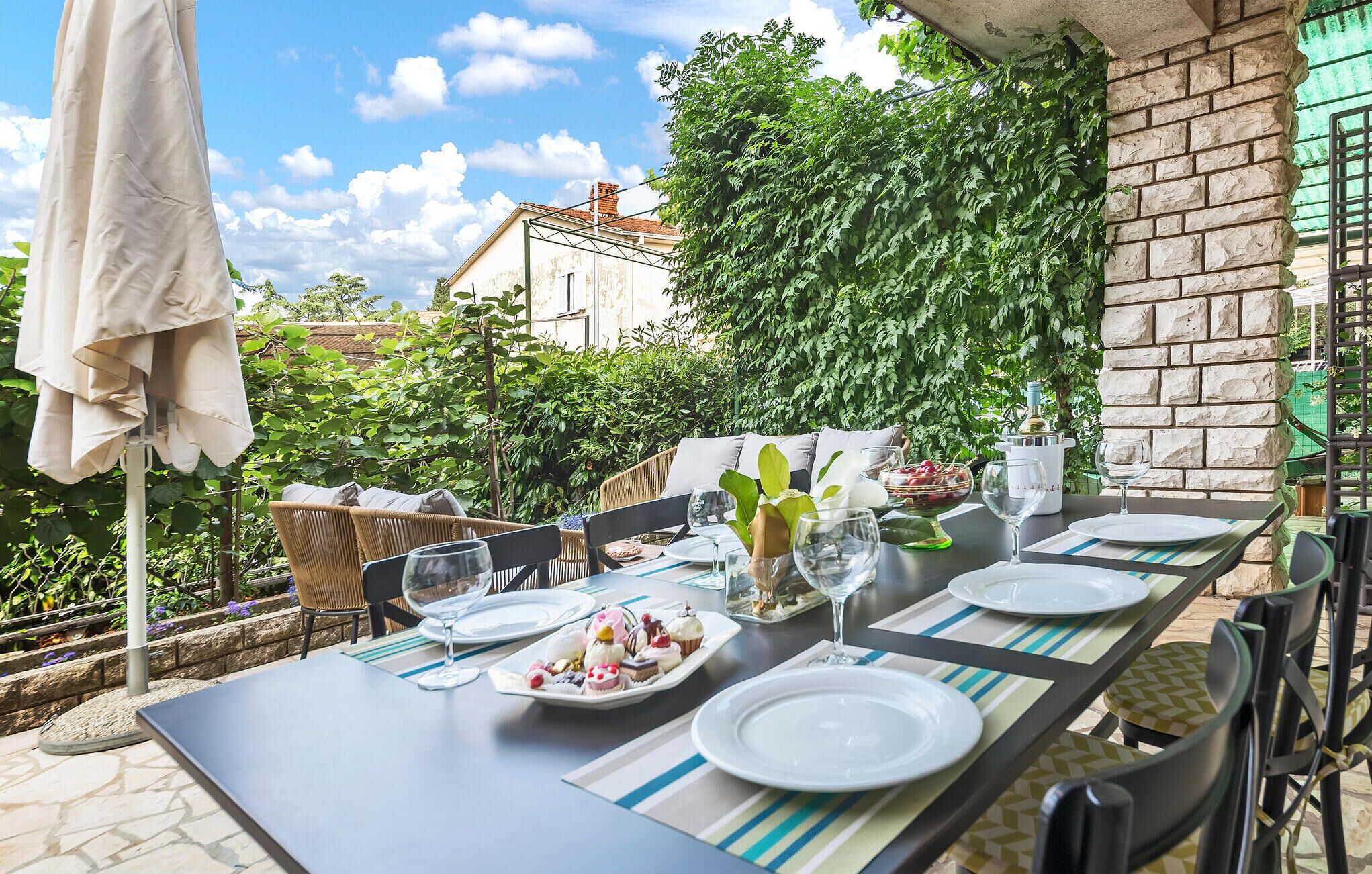 Un espace de restauration en plein air avec une table dressée pour quatre personnes, entouré de verdure et bordé d’un mur de briques.