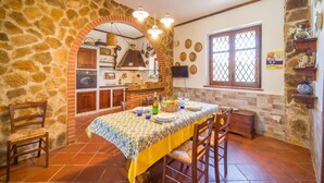 Cuina amb parets de pedra, terra de rajola i zona de menjador amb taula preparada per a quatre.
