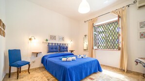 Un dormitori amb un llit, una cadira, una taula de nit, una finestra amb cortines i un aire condicionat fixat a la paret.