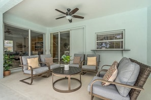 Un espace patio aménagé avec du mobilier d’extérieur, un ventilateur de plafond et une fenêtre équipée de stores.