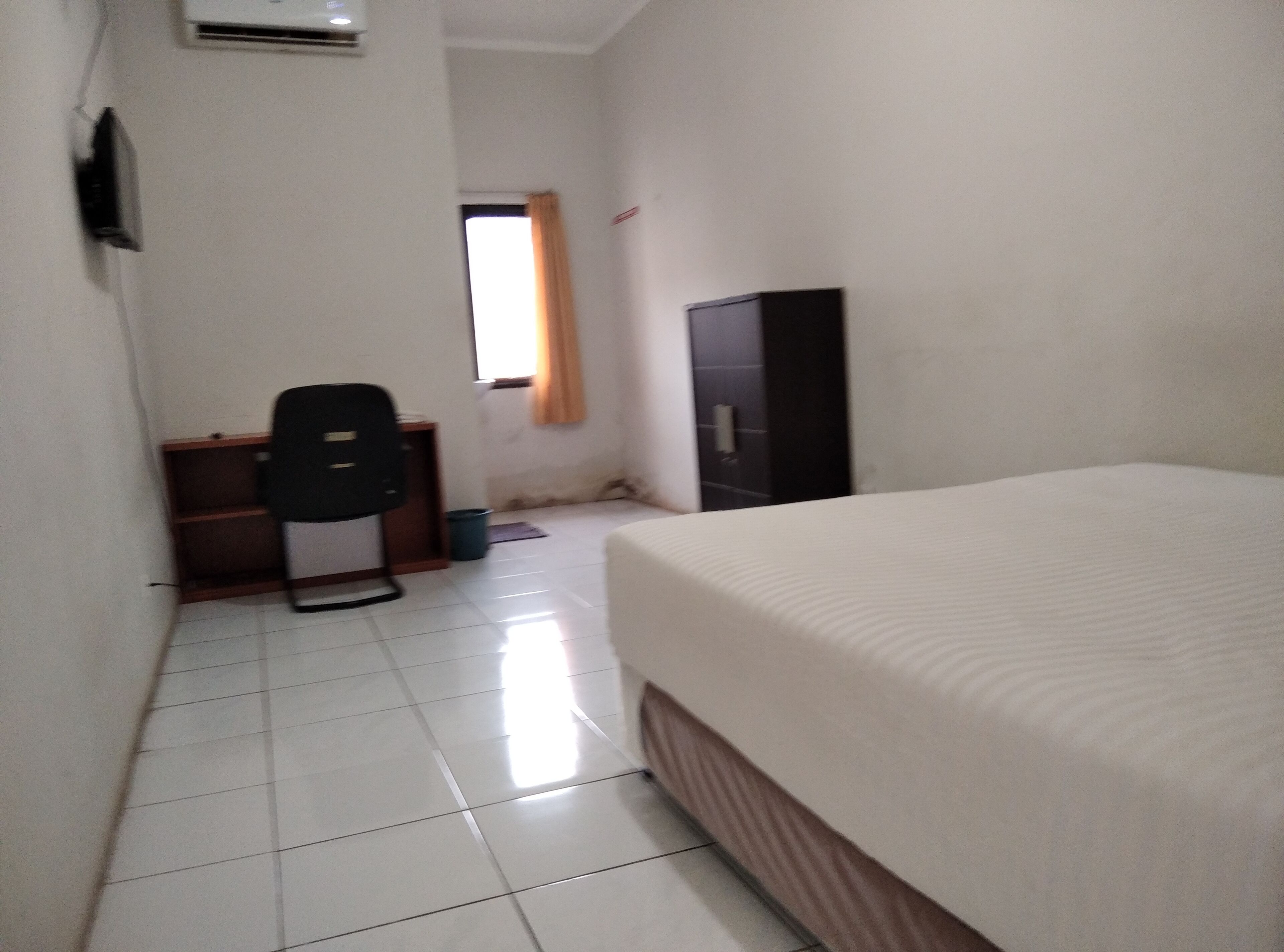 Une chambre d’hôtel avec un lit, un bureau, une chaise, une armoire et une fenêtre.