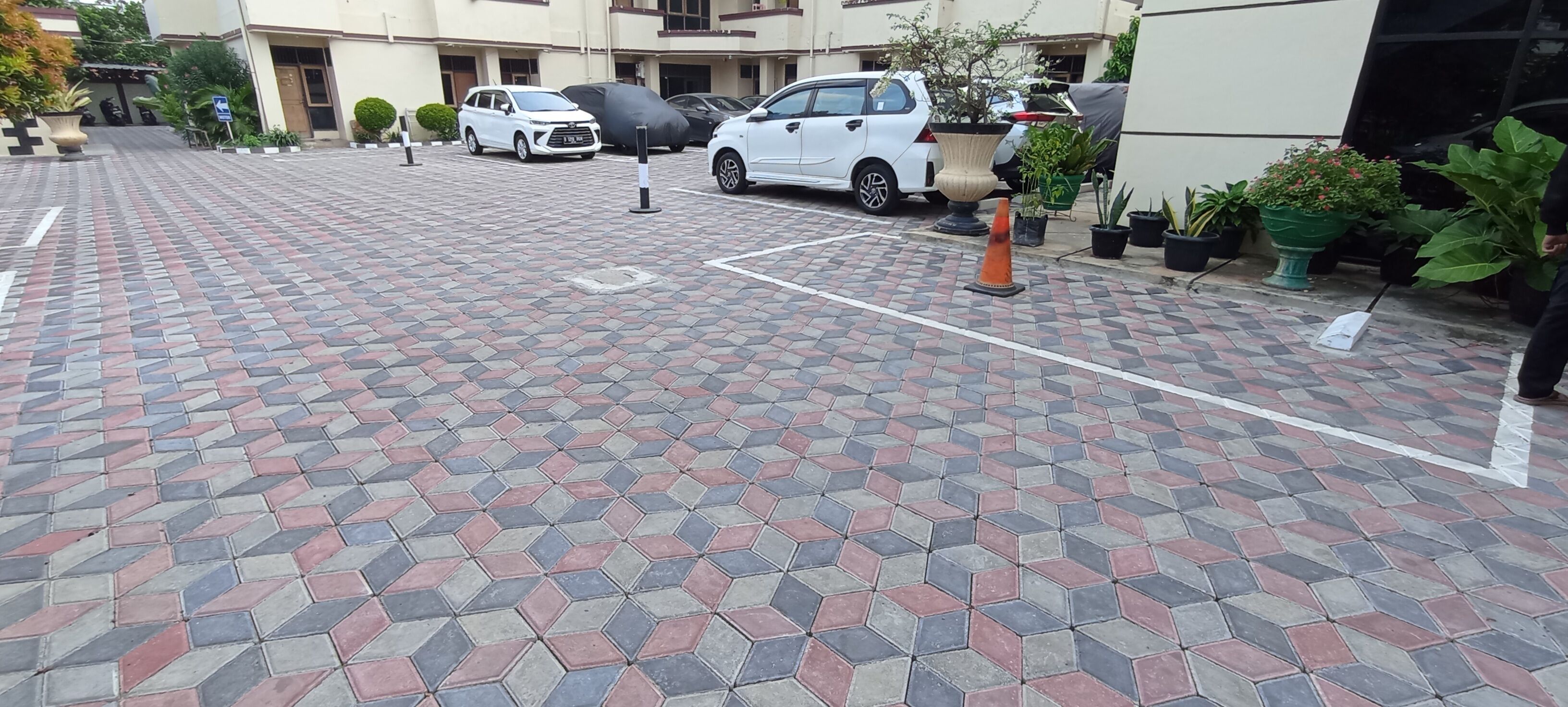 A paved outdoor area with a patterned tile floor, several parked cars, and potted plants.