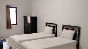 A room with two single beds, a wardrobe, and a window with curtains. - Wisma Anton Soedjarwo (Jakarta)