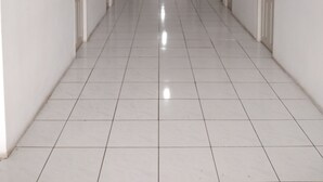 A long, narrow hallway with white tiled floors and walls, doors on both sides, and recessed lighting on the ceiling. - Wisma Anton Soedjarwo (Jakarta)