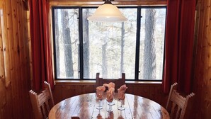 Una mesa de madera para comer con sillas, una araña y una ventana con cortinas.