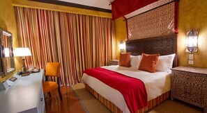 Habitación de hotel con cama, escritorio, silla y una mesita de noche estampada.