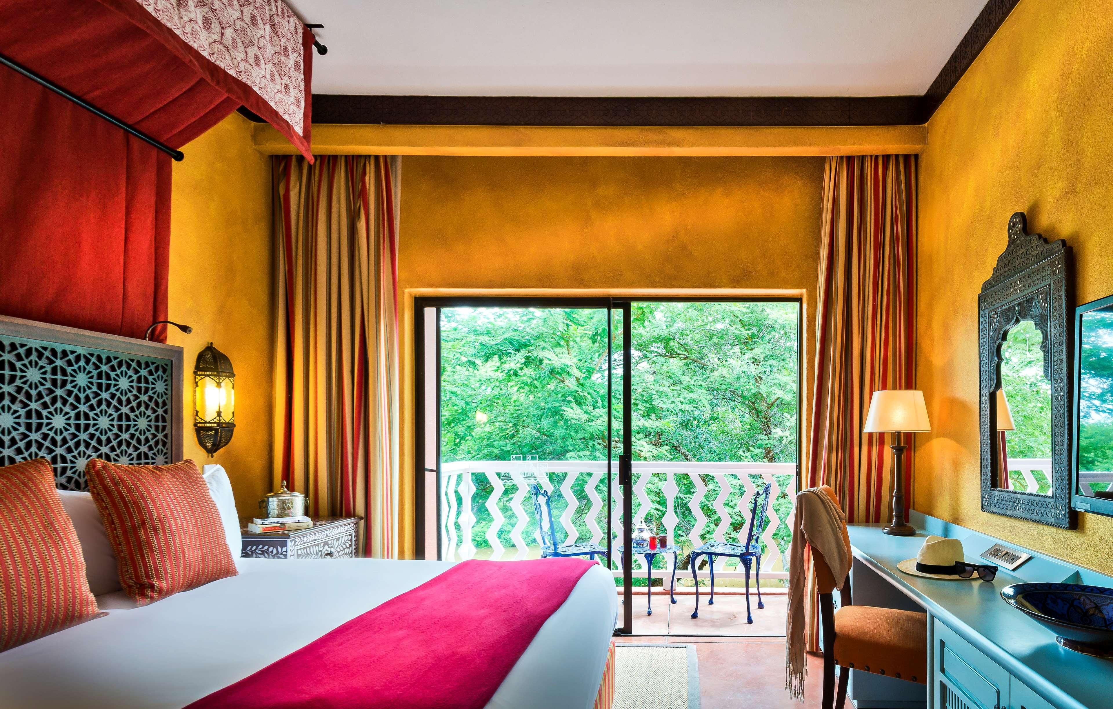 Camera d'albergo con un letto, una scrivania, una sedia, un balcone con vista sul verde e una parete decorativa.