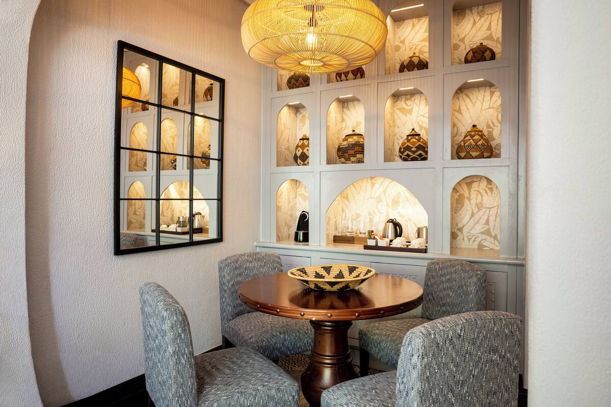 A dining area with a round table, four upholstered chairs, a decorative wall with multiple arched niches, and a hanging light fixture.