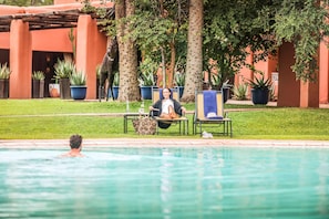 A pool area with lounge chairs and potted plants. - Avani Victoria Falls Resort (Livingstone)