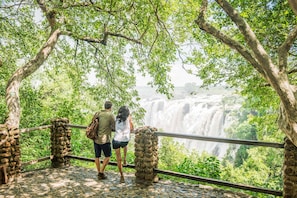 Un couple se tient sur un pont de pierre, d’où l’on aperçoit une cascade, le tout étant entouré d’une végétation luxuriante.