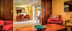 Habitación de hotel con una mesa de centro de madera, un sofá rojo, un área de comedor con sillas y un espejo grande.