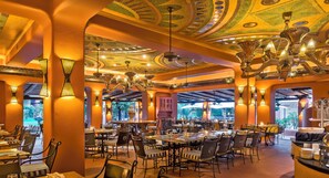 Un restaurante con techo alto, candelabros ornamentales y vistas al verdor exterior.