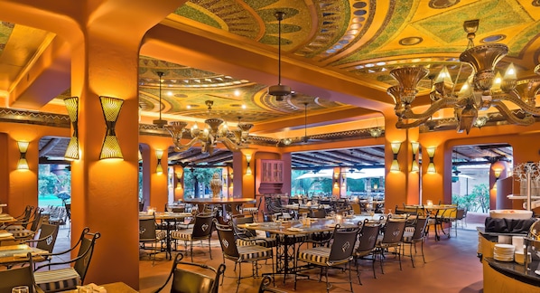 A restaurant with a high ceiling, ornate chandeliers, and a view of greenery outside. - Avani Victoria Falls Resort (Livingstone)