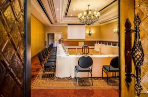 A conference room with a long table, chairs, a chandelier, and a projector screen. - Avani Victoria Falls Resort (Livingstone)