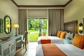 Habitación de hotel con dos camas, un escritorio, una silla y vistas a un jardín.