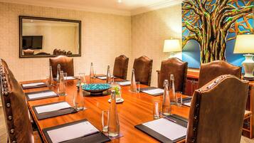 A conference room with a long table, leather chairs, a large mirror, and a colorful tree painting.