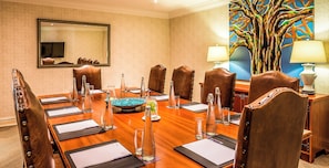 A conference room with a long table, leather chairs, a large mirror, and a colorful tree painting. - Avani Victoria Falls Resort (Livingstone)