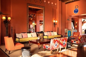 A room with a sofa, chairs, a table, and a mirror. - Avani Victoria Falls Resort (Livingstone)