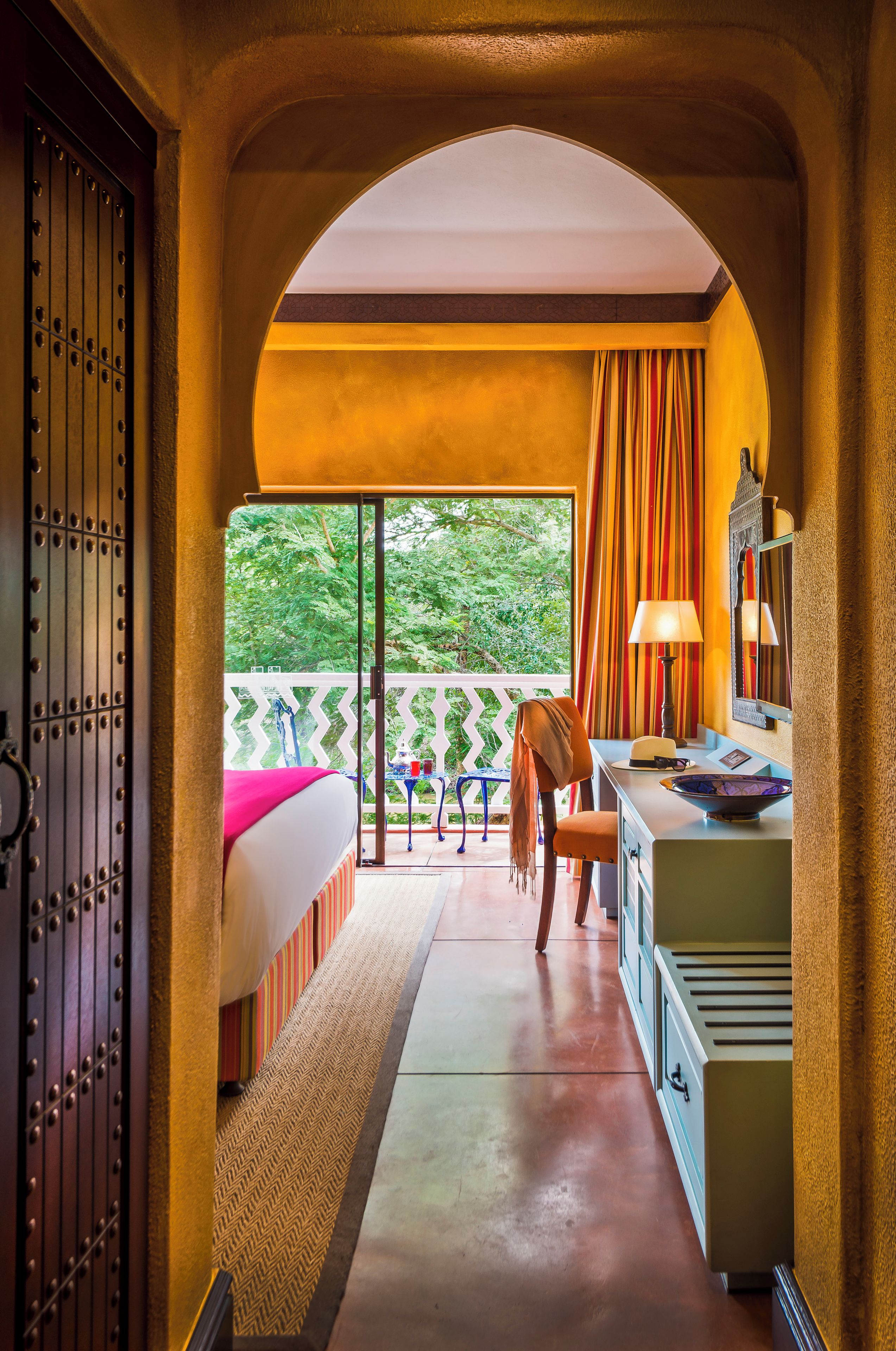 Une chambre avec un lit, un bureau, une chaise et une vue sur la verdure environnante.