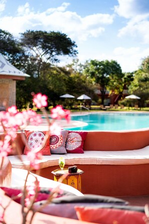 Un área de descanso junto a la piscina con vistas al agua, rodeada de árboles y sombrillas.