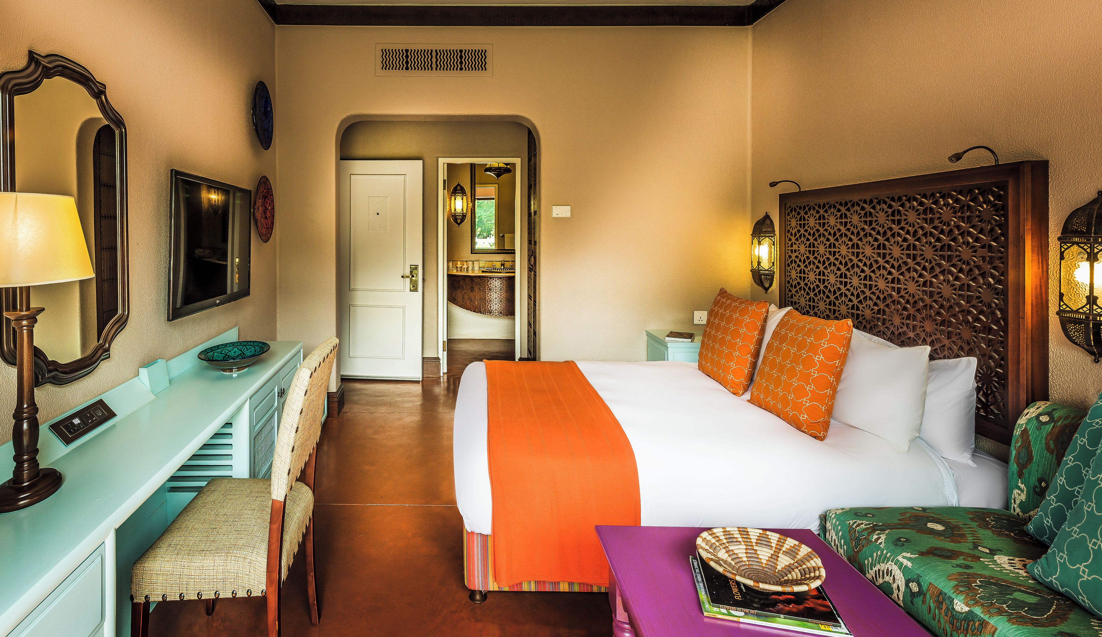 Une chambre d’hôtel comprenant un lit, un bureau, une chaise, une lampe et un panneau décoratif mural.