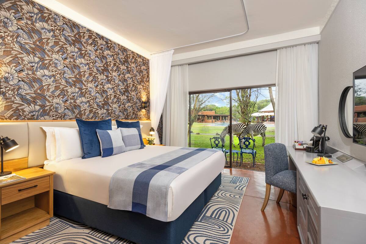 A modern hotel room with a large bed, a desk, and a view of the outdoors.