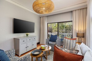Una sala de estar moderna con una televisión de pantalla plana, un sofá, una mesa de centro con frutas y un balcón con cortinas.