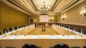 Un salón de conferencias con una larga mesa, sillas, una pantalla de proyector y una araña.